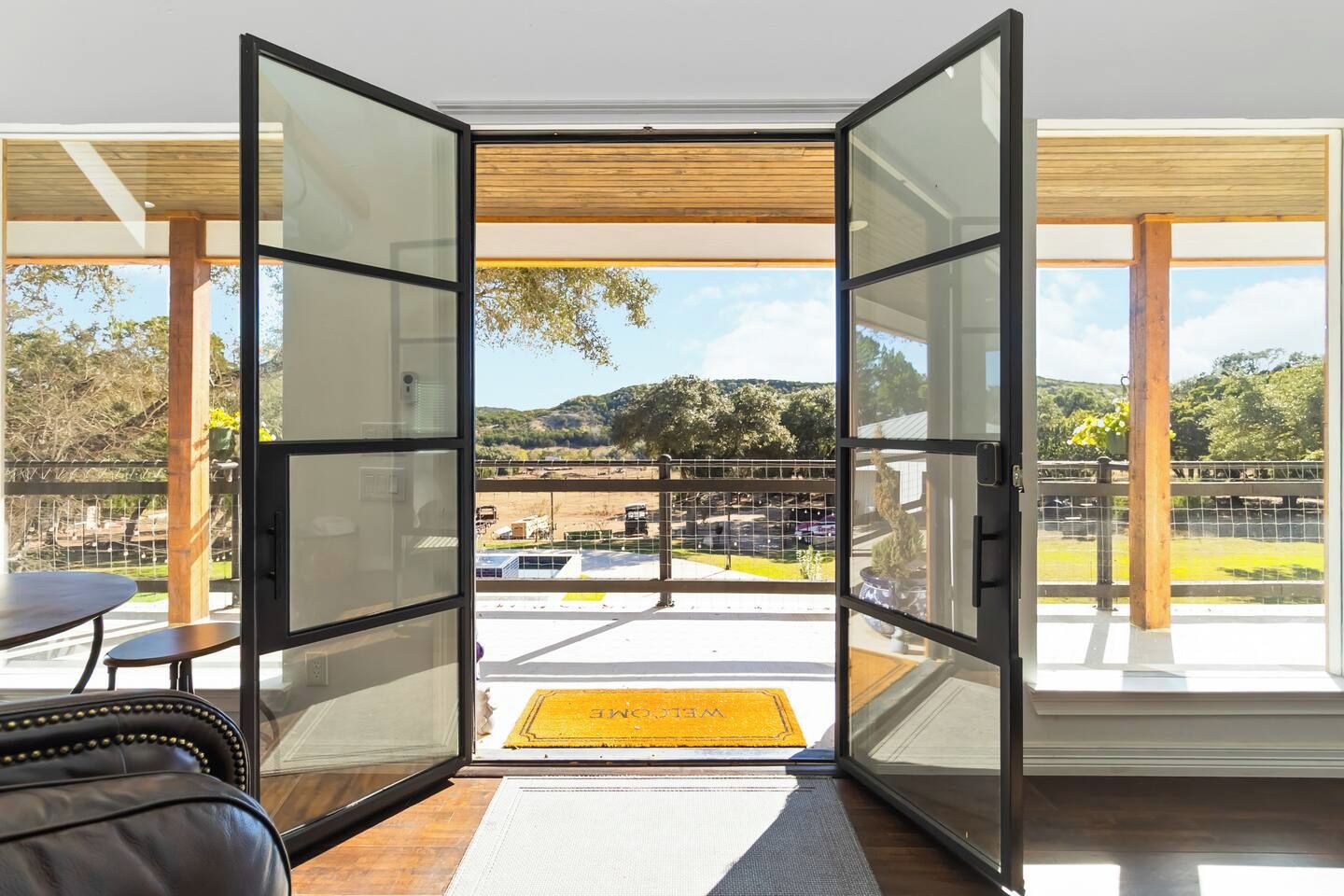 A modern room with a glass door leading to a balcony with a view of a parking area and hills.