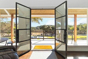 A modern room with a glass door leading to a balcony with a view of a parking area and hills. - 2 Homes on Boerne Acreage w/ Fire Pit & Hill Views (Boerne)