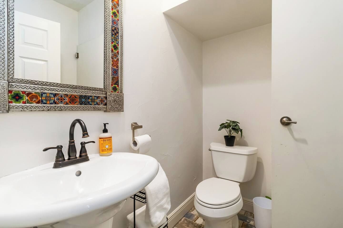 A bathroom with a white sink, a mirror with a decorative frame, a toilet, and a potted plant.