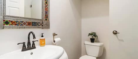 A bathroom with a white sink, a mirror with a decorative frame, a toilet, and a potted plant.