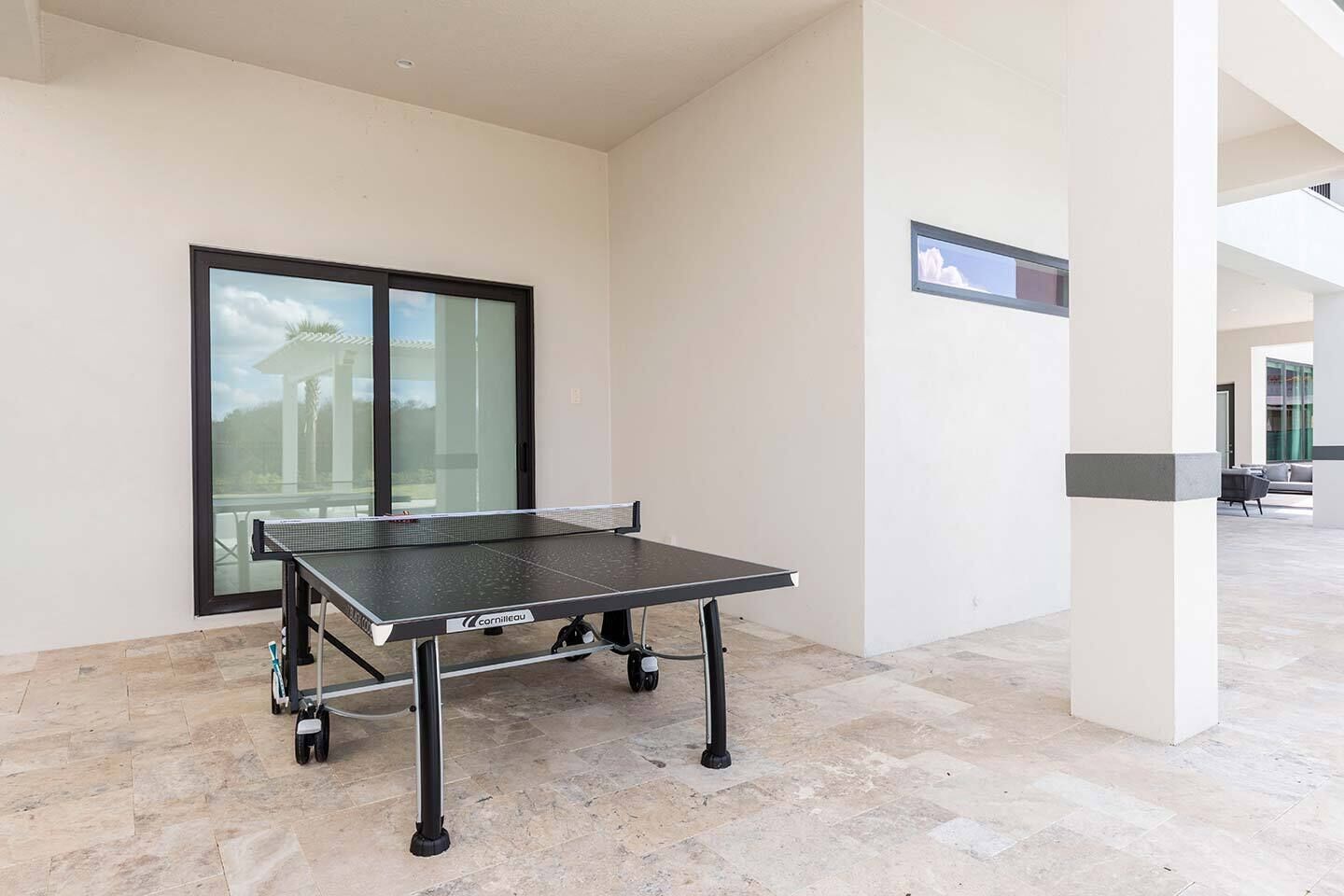 A ping pong table in a spacious, modern indoor area with a large window and a view of a building outside.