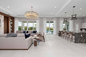 A spacious living area with a modern sofa, a dining area with bar stools, and a kitchen with a marble countertop. - The Dream Mansion | Luxe 10BR w/ Private Pool, Spa, Sauna, Theater Near Disney (Kissimmee)