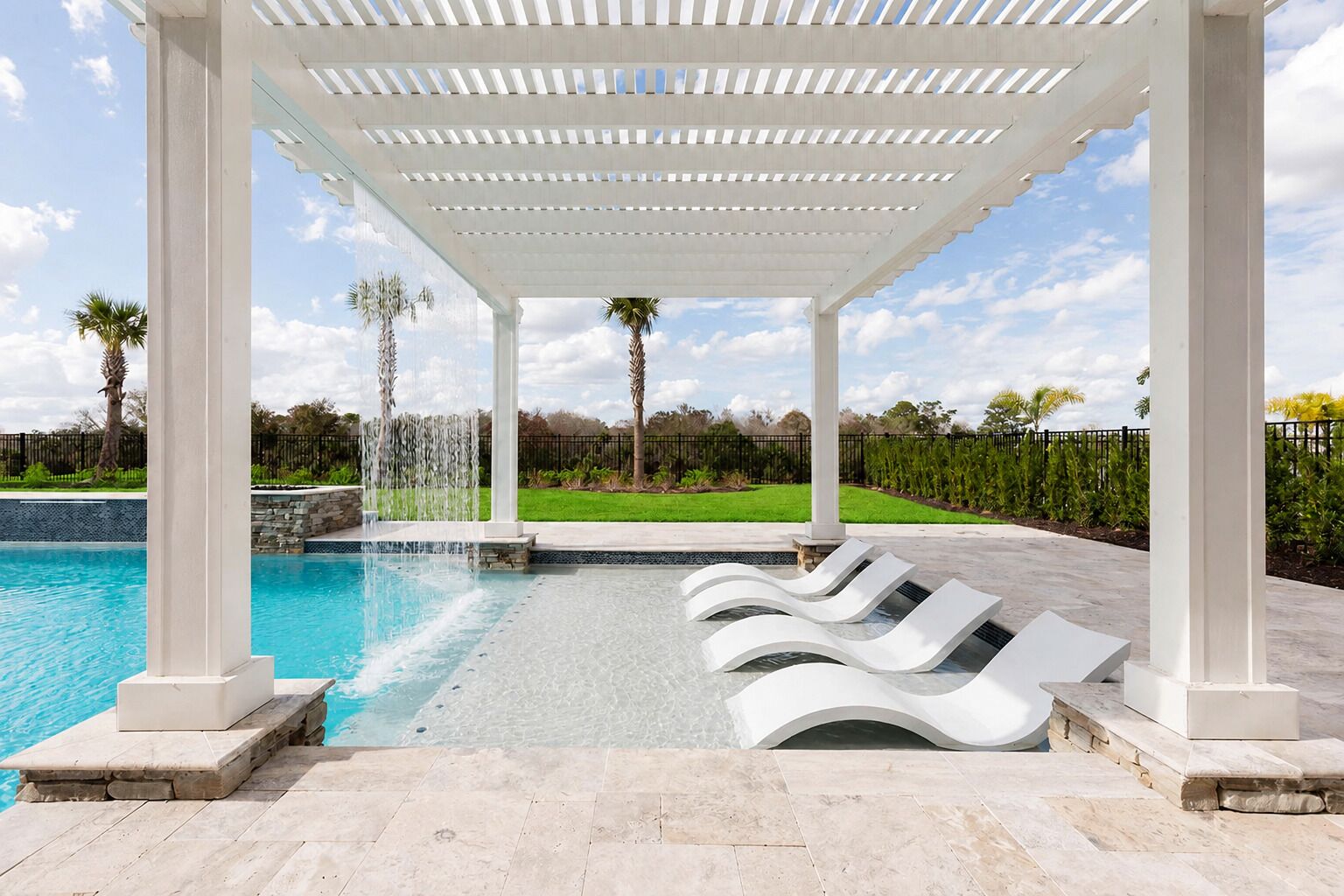 Un área de piscina con una pérgola blanca, sillas de descanso y una fuente de agua.