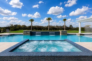 A swimming pool with a waterfall feature, surrounded by a white pergola and palm trees. - The Dream Mansion | Luxe 10BR w/ Private Pool, Spa, Sauna, Theater Near Disney (Kissimmee)