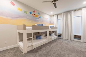Ein Kinderzimmer mit Etagenbetten, Deckenventilator und Wandbild mit dem Schriftzug "Coco".