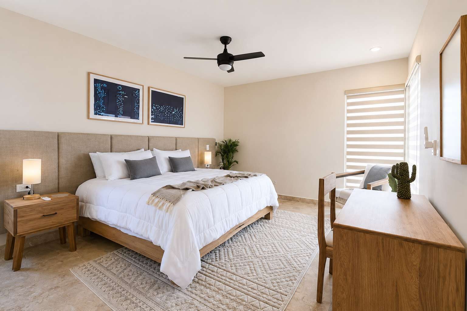 Une chambre à coucher comprenant un lit, des tables de chevet, un bureau, une chaise, un ventilateur de plafond et deux tableaux accrochés au mur.