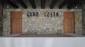 Ein Empfangsbereich mit einer Steinwand, Holztüren und einem Schild mit der Aufschrift 'CABO COSTA'.
