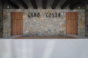Un espace d’accueil avec un mur en pierre, des portes en bois et une plaque nominative portant l’inscription « CABO COSTA ».