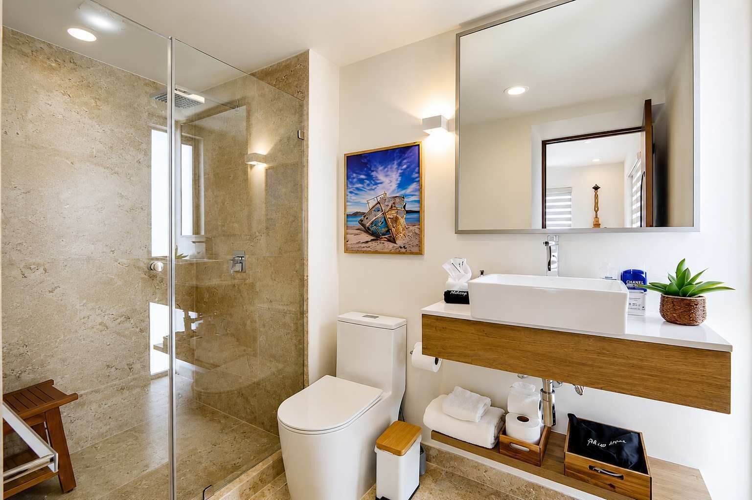 Ein modernes Badezimmer mit einer ein Glasfachwerk-Duschkabine, einer weißen Toilette, einem Waschbecken mit einem Holzschrank und einem Spiegel über dem Waschbecken.