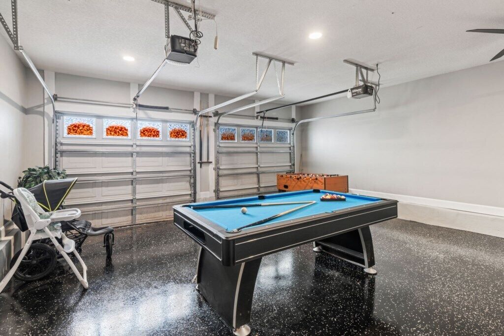 A pool table in a room with a garage door and a projector mounted on the ceiling.
