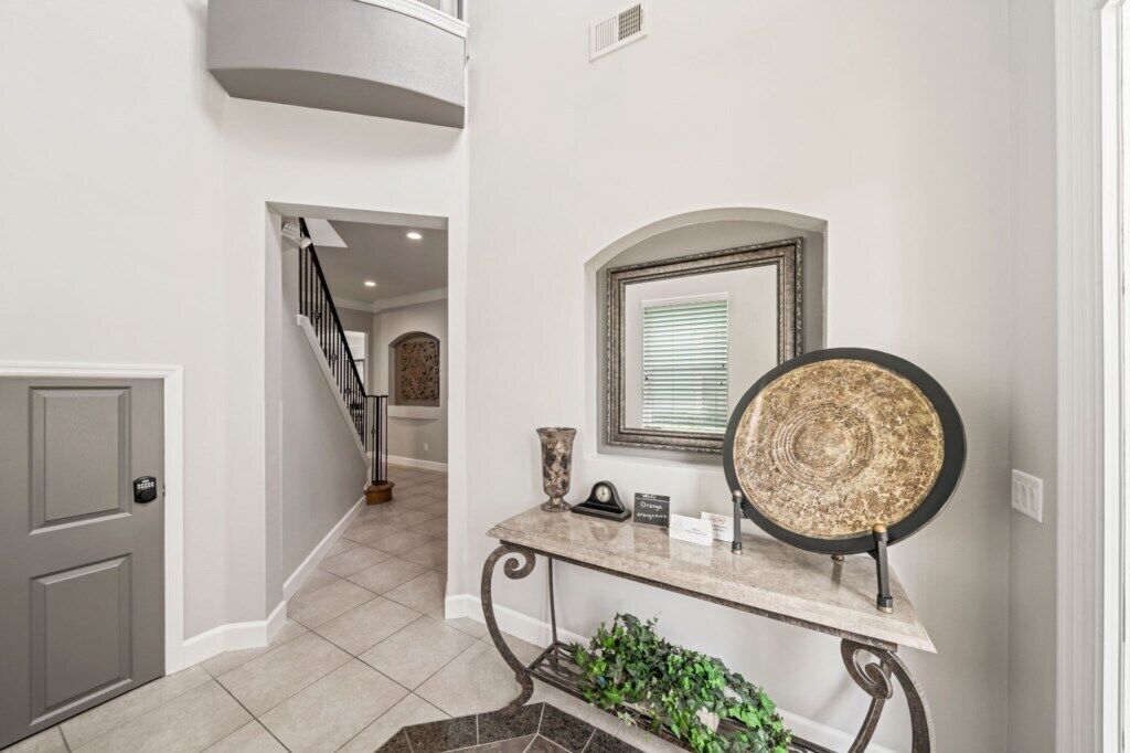 A hallway with a grey door, a marble console table with a decorative plate, and a staircase leading to an upper level.