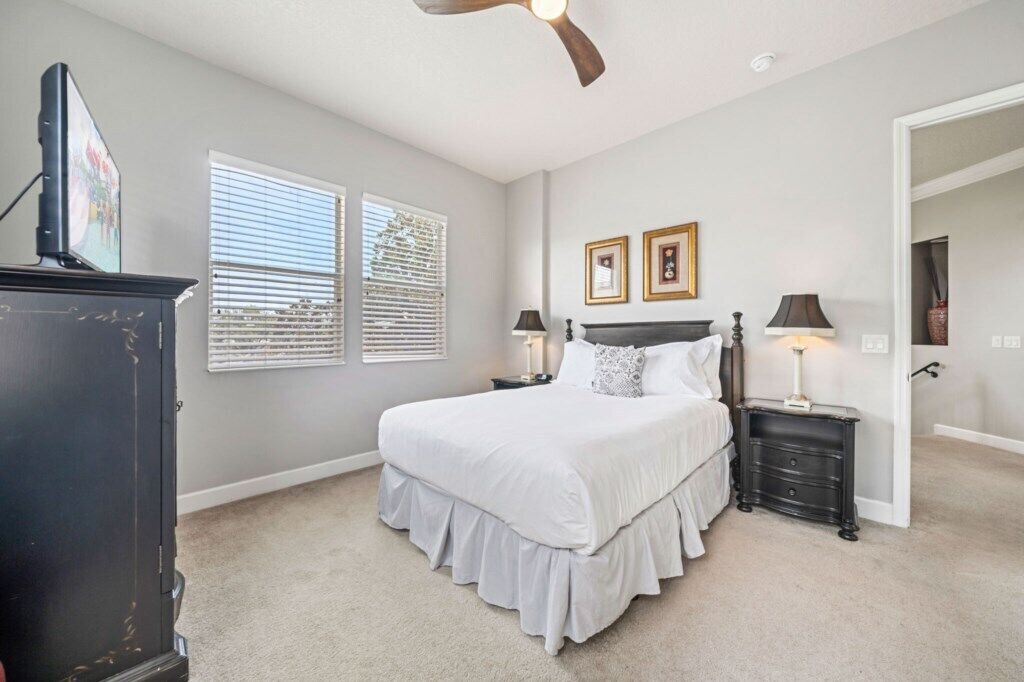 A bedroom with a bed, two bedside tables, a ceiling fan, and a window with blinds.