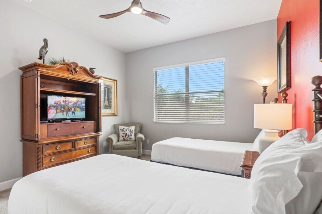 Habitación de hotel con cama, televisión, silla y ventana con persianas.