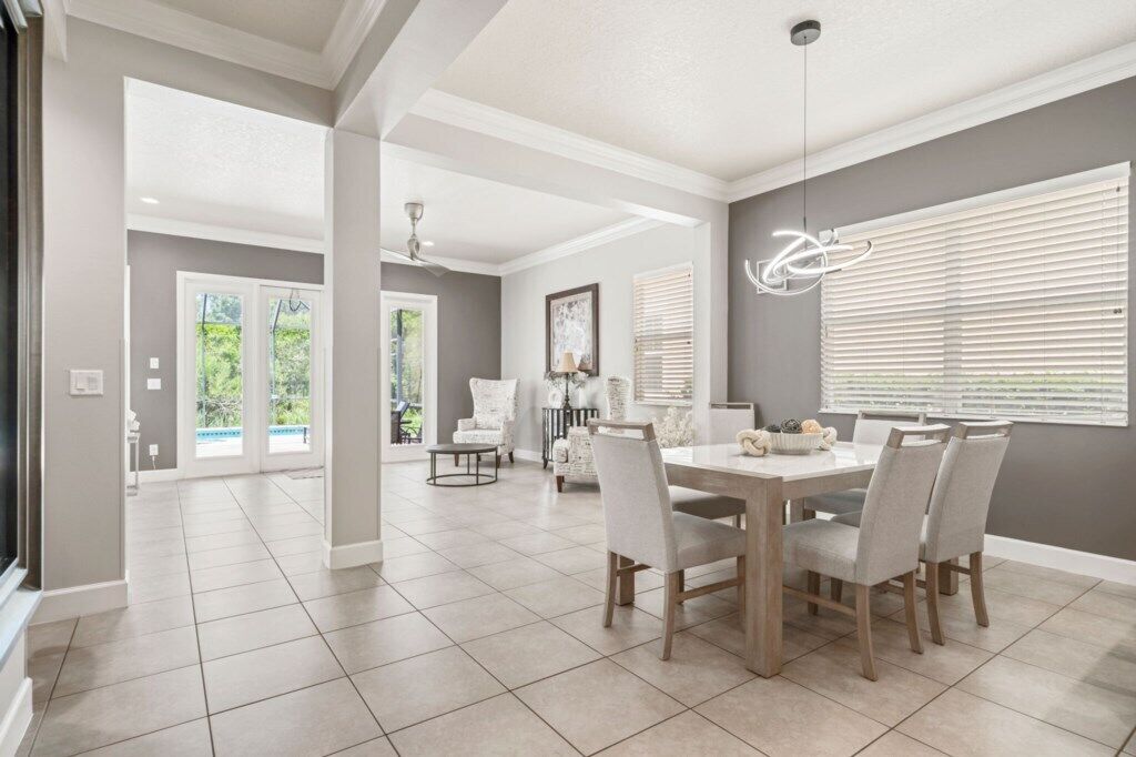 A spacious dining area with a large table and chairs, a ceiling fan, and a view of the outdoors through large windows.