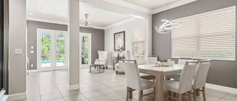 A spacious dining area with a large table and chairs, a ceiling fan, and a view of the outdoors through large windows.