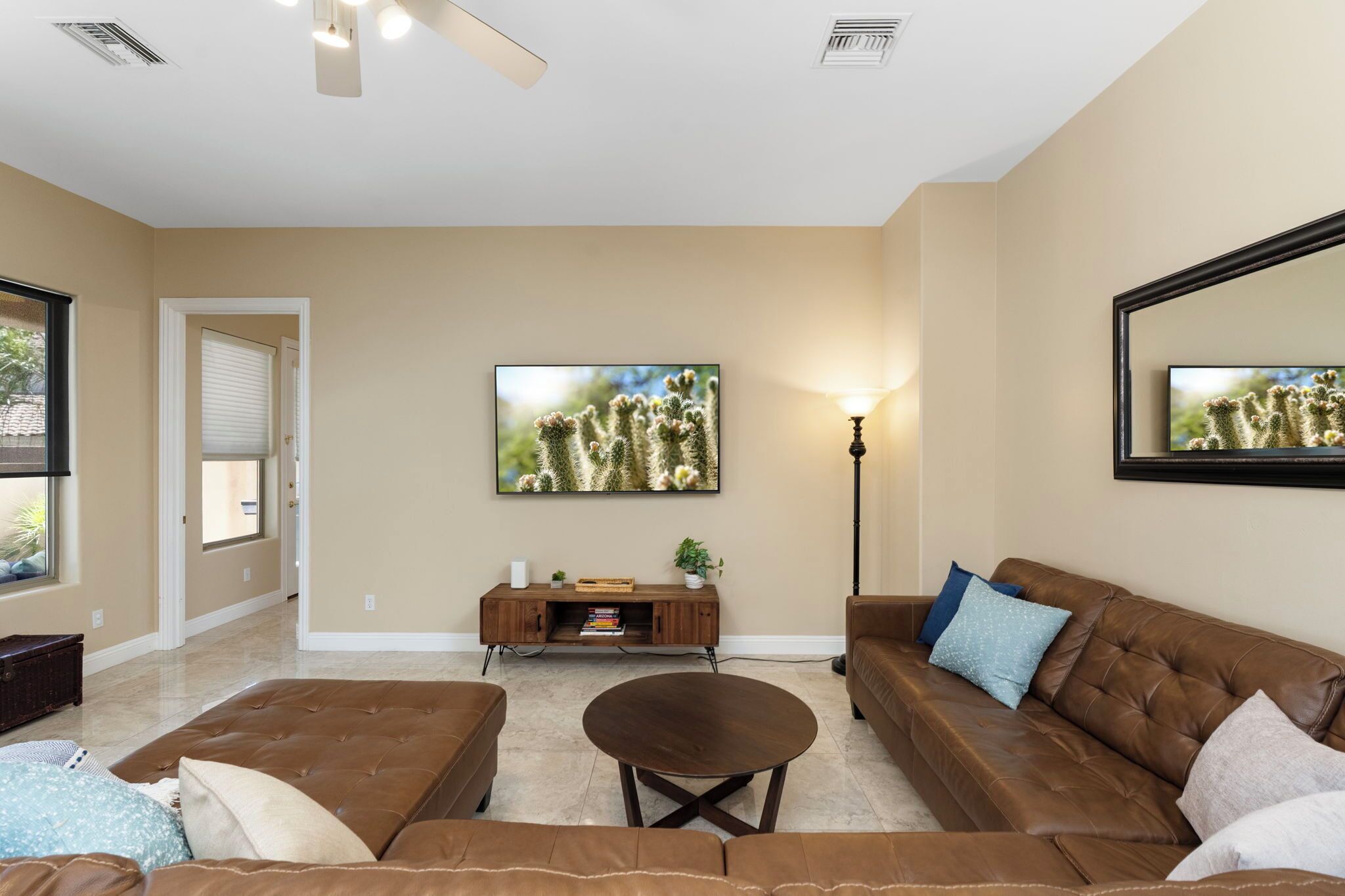 A living room with a brown leather sofa, a round coffee table, and a large painting of cacti on the wall.