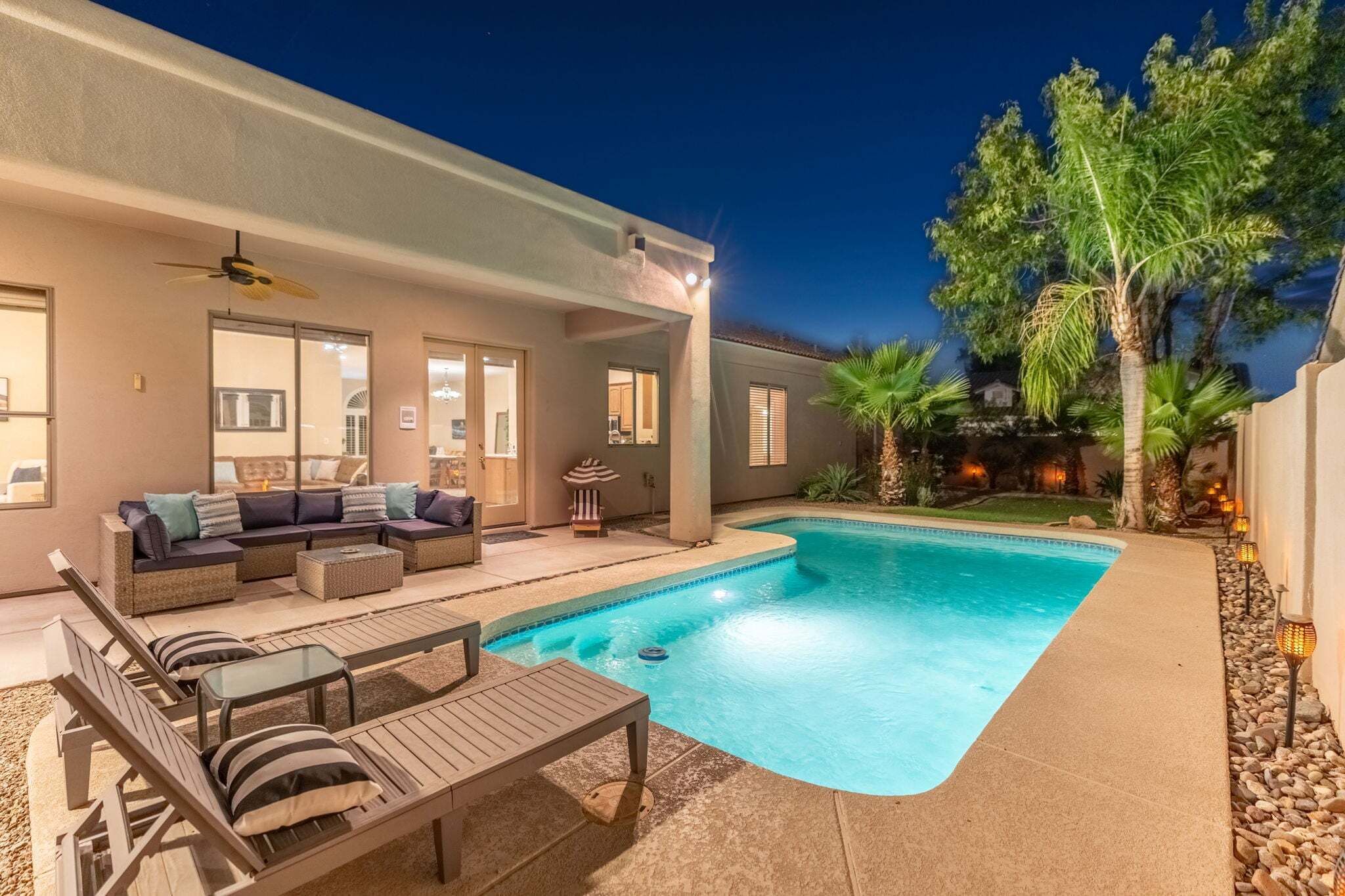 A swimming pool with lounge chairs and a sofa, surrounded by a landscaped garden with palm trees.
