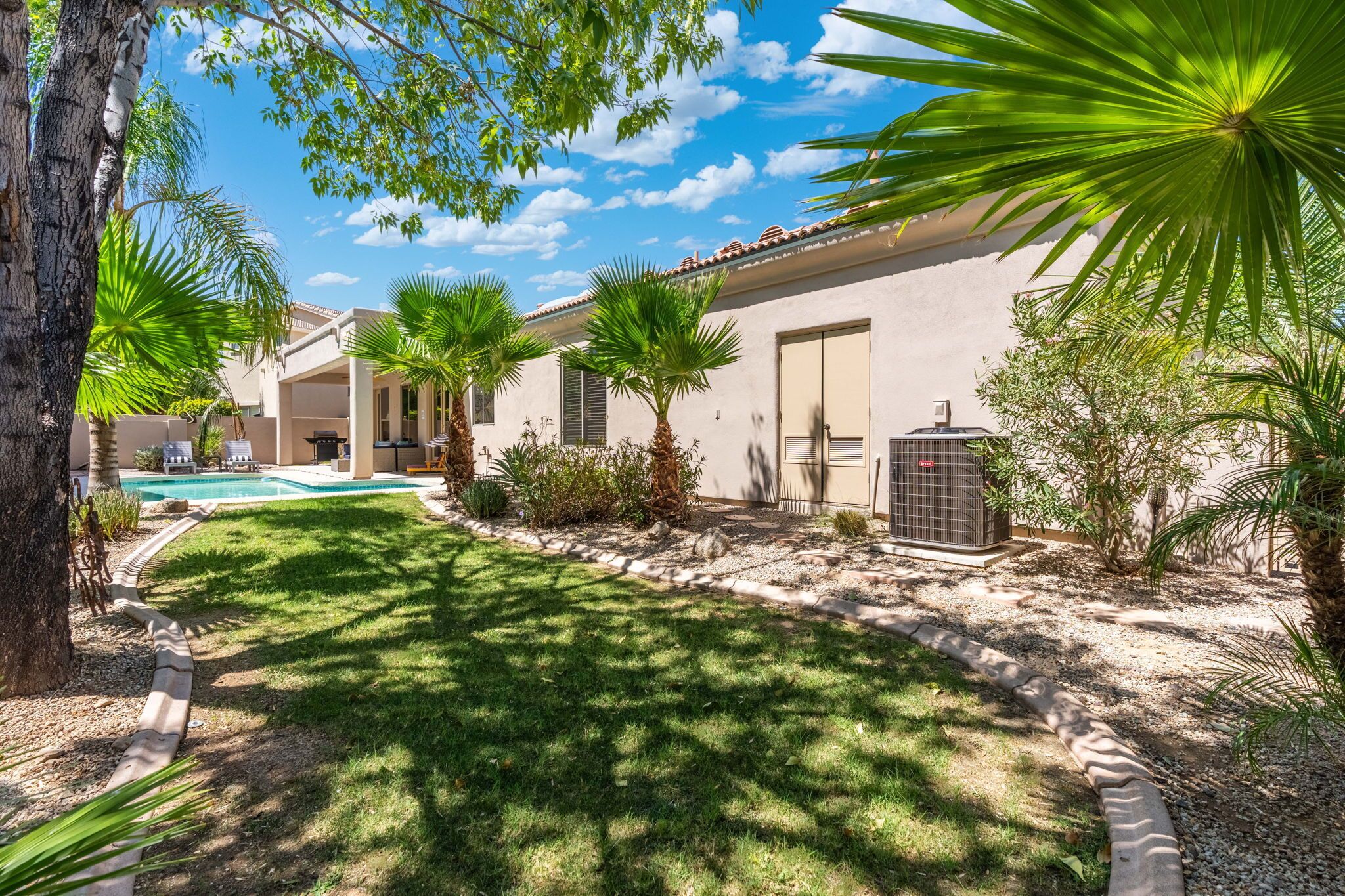 A residential property with a swimming pool, palm trees, and a covered patio area.
