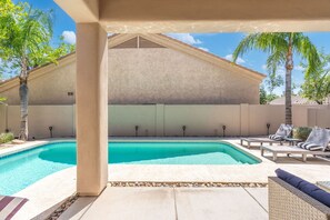 Ein Schwimmbecken mit überdachter Terrasse, Liegestühlen und Palmen.