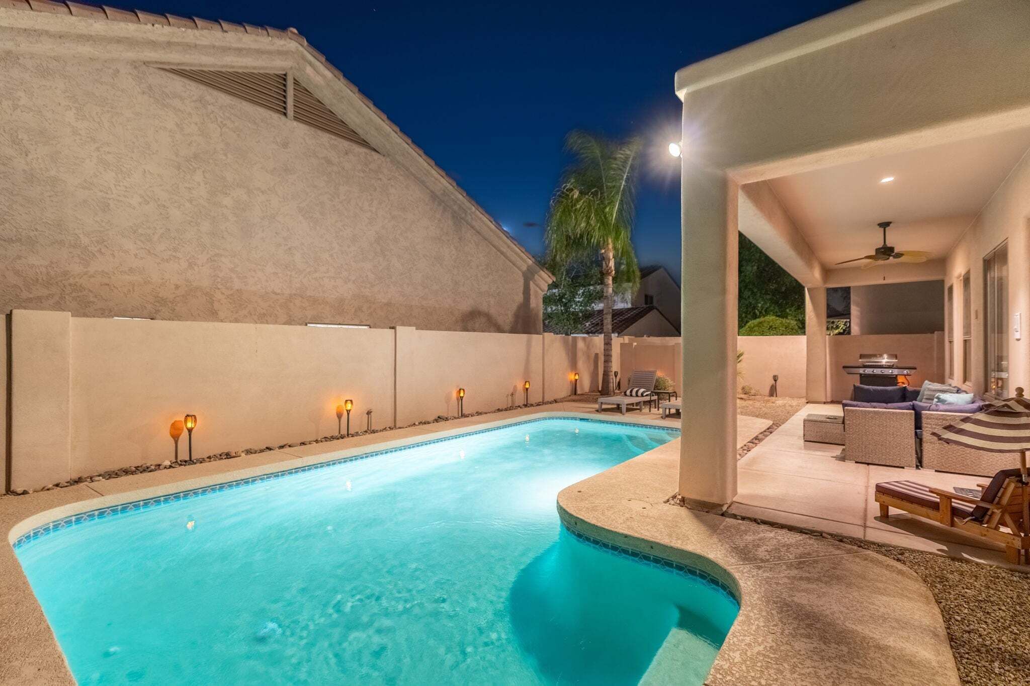 Une piscine à bords incurvés, entourée d’un patio aménagé avec des sièges et un barbecue.
