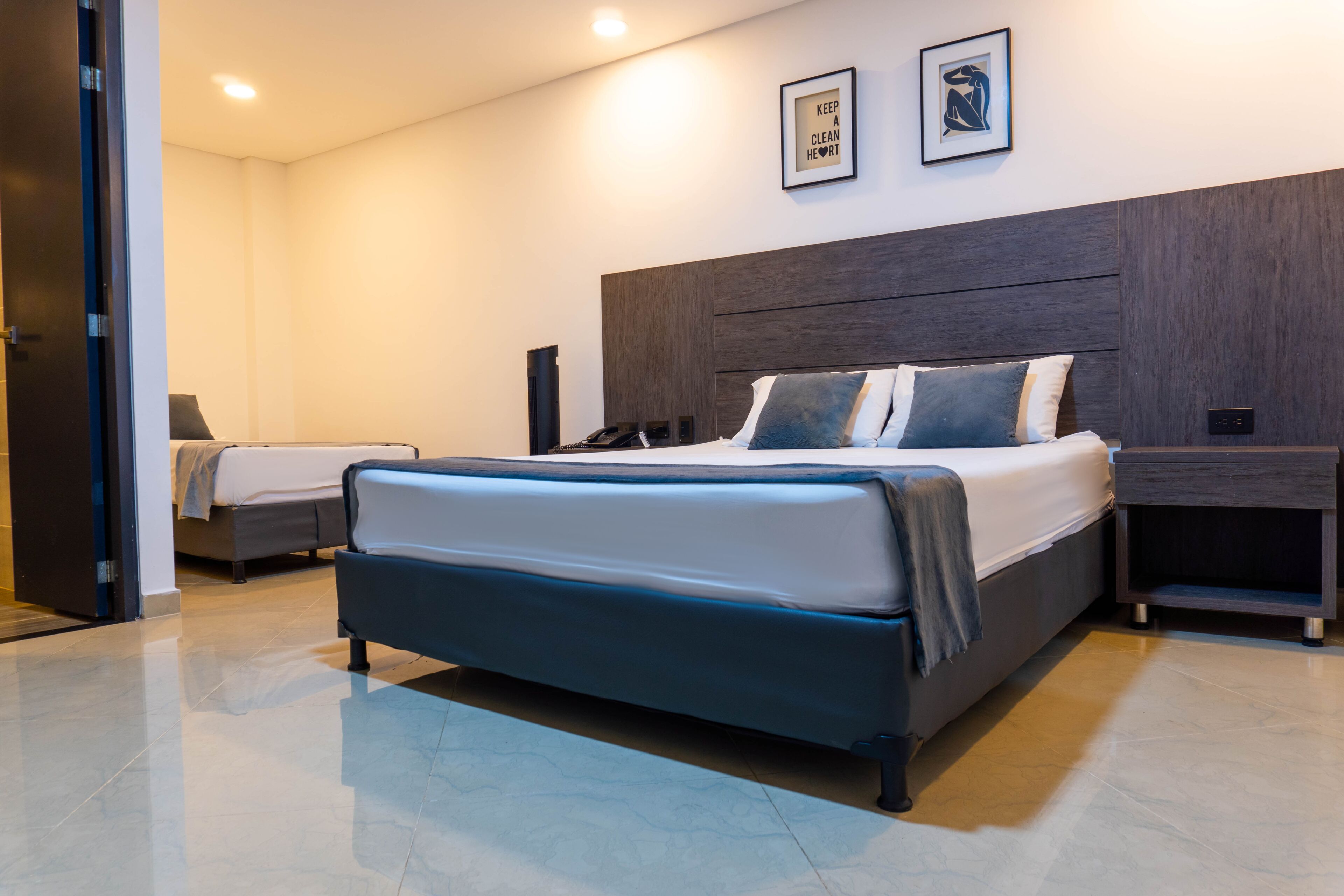 A modern hotel room with a large bed, bedside tables, a desk, and a headboard.