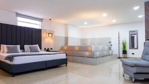 Un dormitorio moderno con una cama grande, una mesita de noche, un banco empotrado y una zona de estar con una silla.