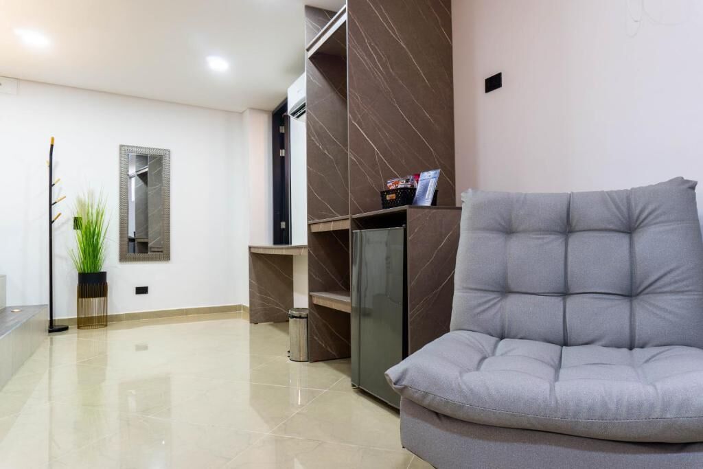 A modern living room with a grey sofa, a small table, a plant, and a wall-mounted mirror.