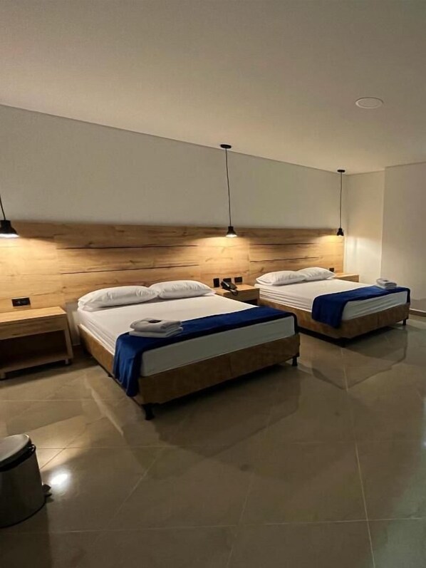 A hotel room with two beds, a wooden headboard, bedside tables, and a trash bin. - California City Hotel (Medellín)