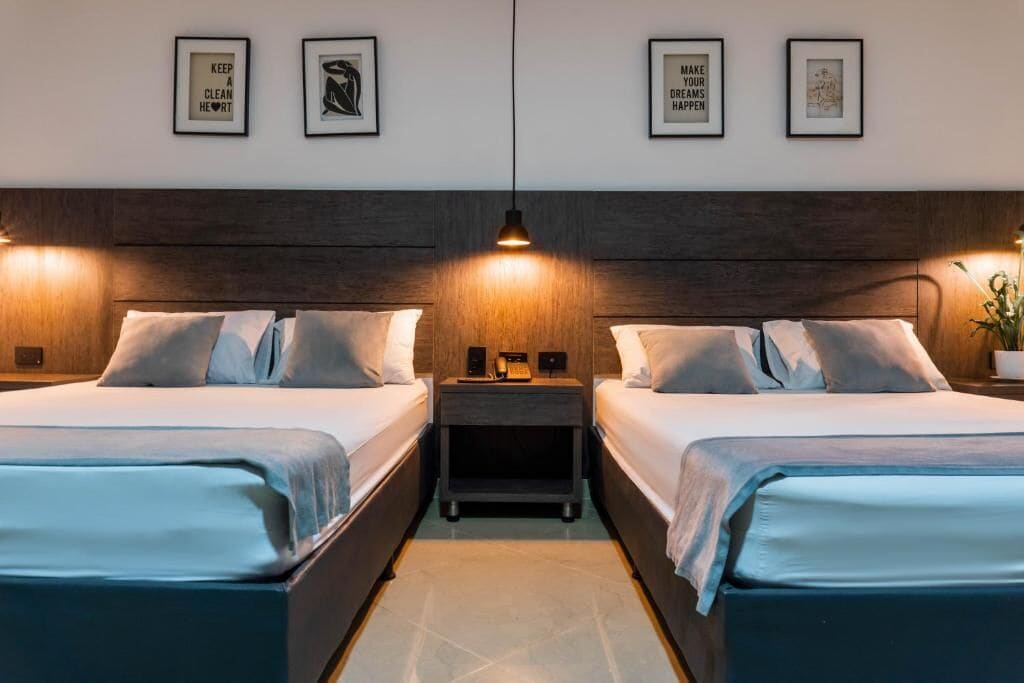 A hotel room with two beds, a nightstand, a lamp, and framed motivational quotes on the wall.