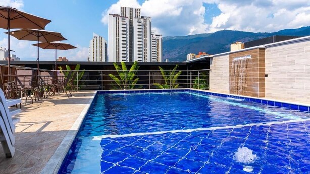 Una piscina en la azotea con vistas despejadas a edificios altos y montañas al fondo.