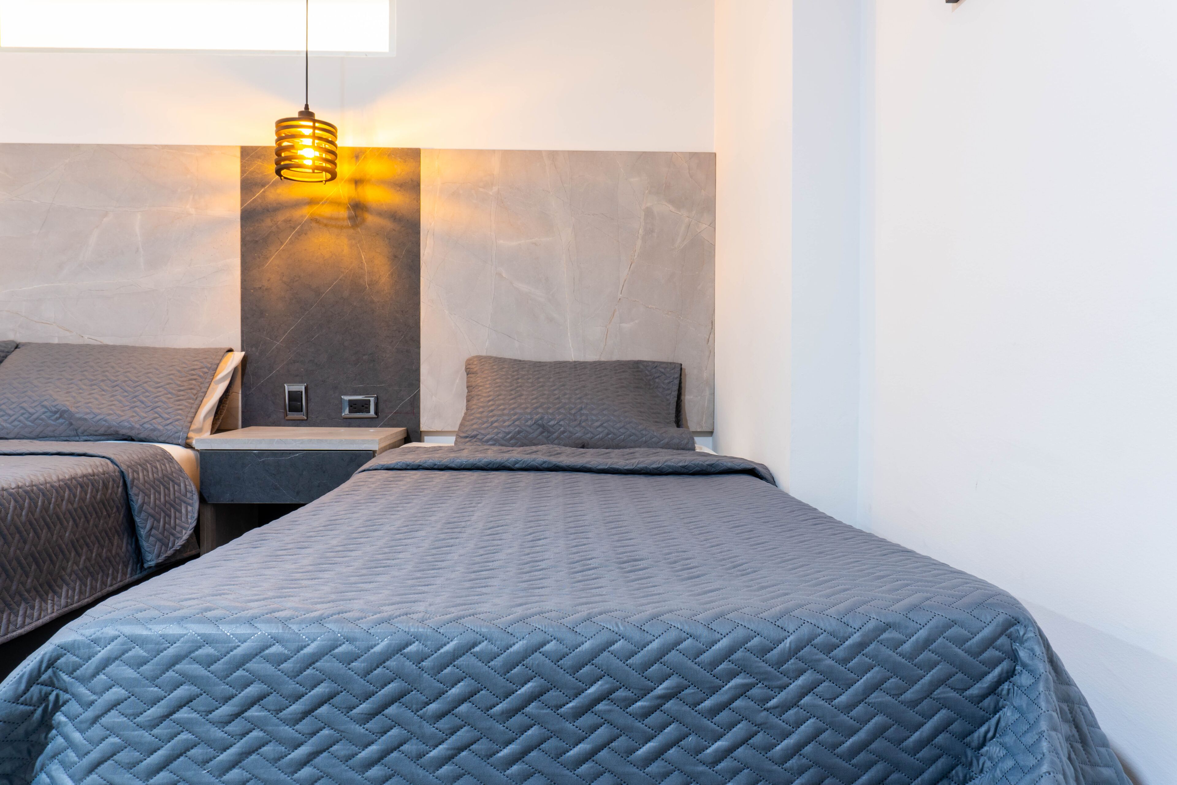 A modern hotel room with two beds, a wall-mounted light fixture, and a large window.