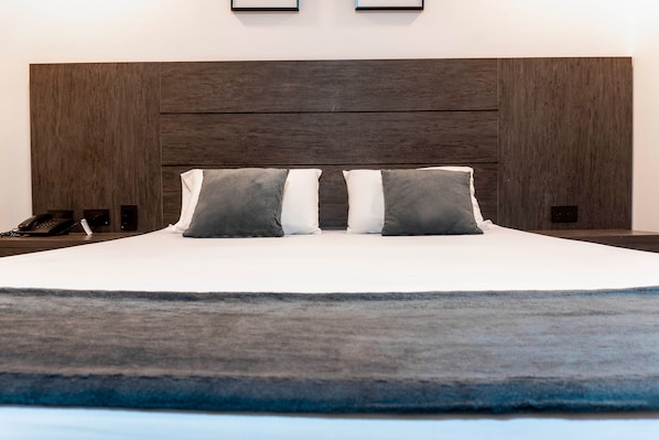 Una cama con cabecera oscura, dos almohadas y una mesita de noche con un teléfono.