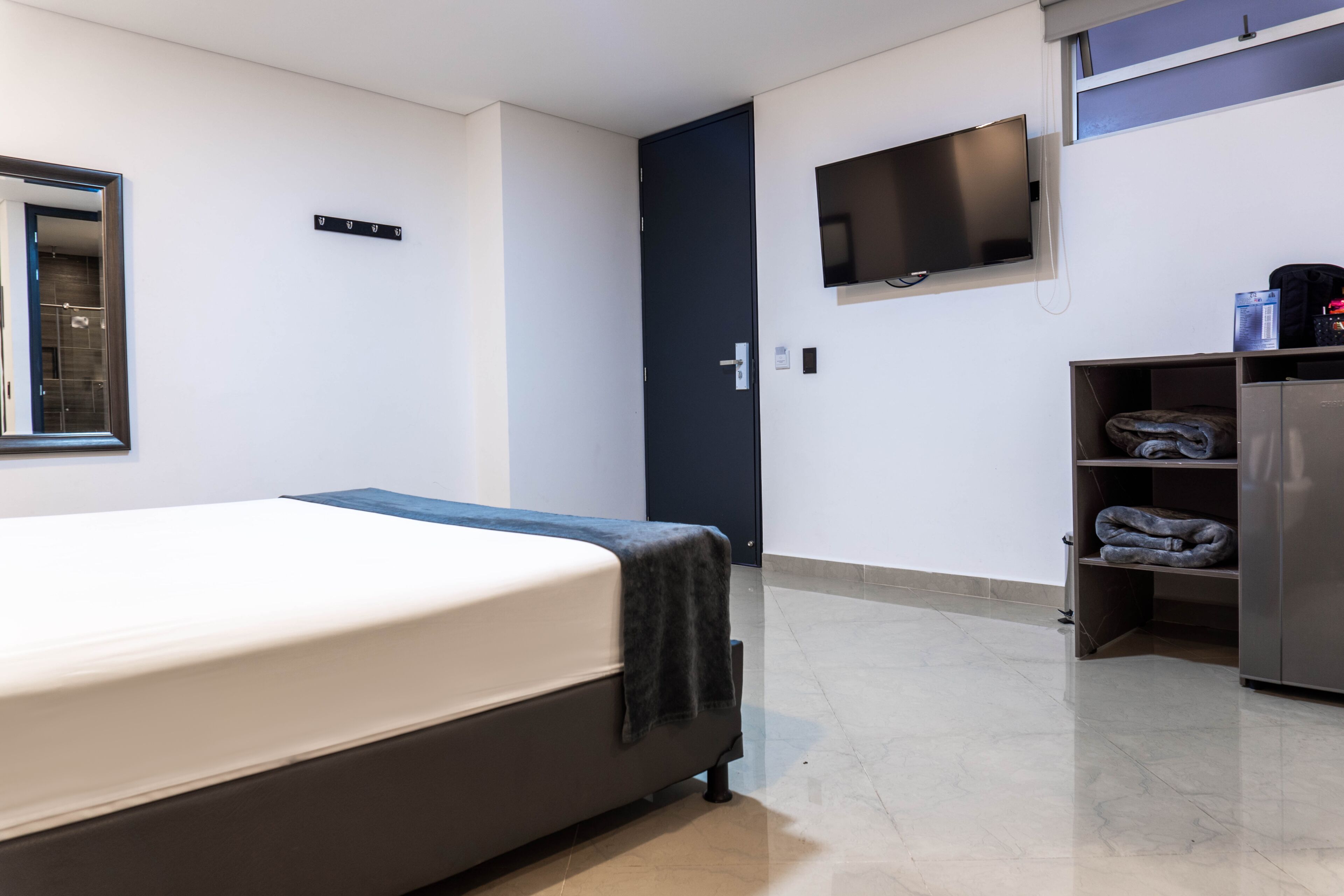 Una habitación de hotel con una cama, un televisor montado en la pared, una puerta y un mueble pequeño.