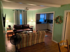 Ein Wohnzimmer mit braunem Ledersofa, einem gestreiften Sofa, einem Ventilator und einem kleinen Tisch mit einer Lampe.