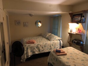 Une chambre avec deux lits, un ventilateur de plafond, un miroir, une étagère avec une lampe et un cadre photo.