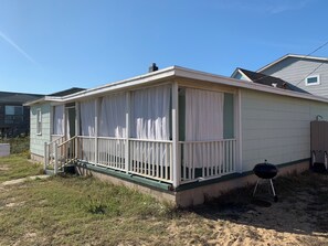 Ein kleines, eingeschossiges Haus mit überdachter Veranda und einer kleinen Terrasse.