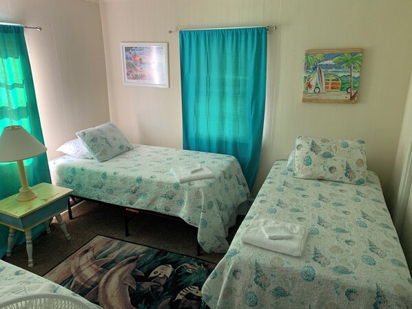 Une chambre avec deux lits, une petite table avec une lampe, un tapis et un tableau au mur.