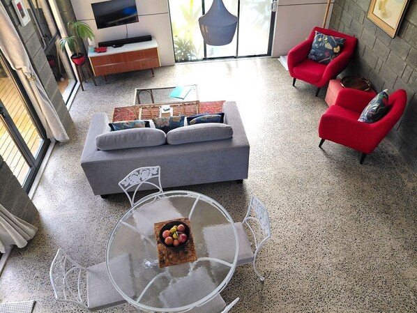Un soggiorno moderno con un divano grigio, poltrone rosse, un tavolino da caffè in vetro con della frutta e una TV a parete.