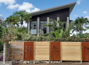 Une maison moderne avec un toit plat, de grandes fenêtres et une clôture en bois ornée de motifs floraux.
