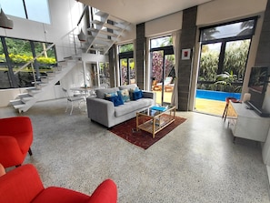 Un intérieur moderne avec un escalier, un canapé gris agrémenté de coussins bleus et un fauteuil rouge.