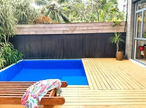 Una piscina con bordo in legno, circondata da piante e un muro scuro.