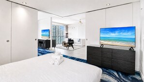 Ein Hotelzimmer mit einem großen Bett, einem Flachbildfernseher, einem Schreibtisch und Meerblick durch das Fenster.
