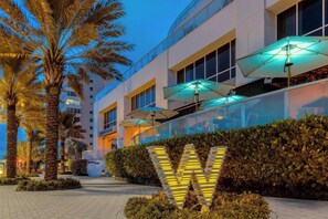A hotel exterior with palm trees, a large illuminated 'W' sign, and outdoor umbrellas. - W Resort | Largest 2BR Corner | 270° Views | PS5 (Fort Lauderdale)