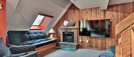 A loft-style living room with a fireplace, a large TV, and a cozy seating area.