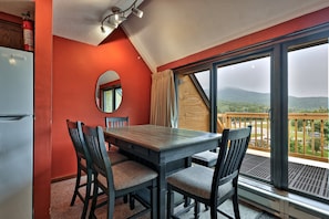 A dining area with a table and chairs, a mirror, and a view of a balcony with a scenic landscape. - The Ski Den at Mountain Green 2BR/2BA (Killington)