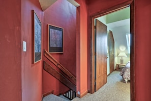A hallway with red walls, wooden doors, and a staircase. - The Ski Den at Mountain Green 2BR/2BA (Killington)