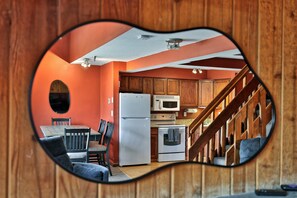 A kitchen with wooden cabinets, a refrigerator, a microwave, an oven, and a dining area with chairs and a table. - The Ski Den at Mountain Green 2BR/2BA (Killington)