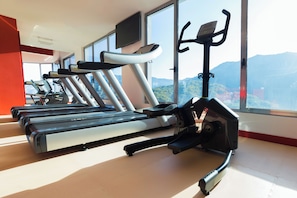 A gym with treadmills and exercise bikes, large windows with a mountain view, and a red accent wall.