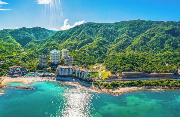 Una località balneare con diversi edifici a grattacielo, una spiaggia e dolci colline verdi sullo sfondo.