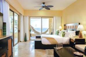 Camera d'albergo con un letto, una scrivania, una sedia, un comodino, una lampada, una ventola a soffitto e vista sull'oceano attraverso ampie finestre.